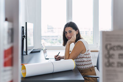 Young businesswoman sitting with hand on chin in front of desktop