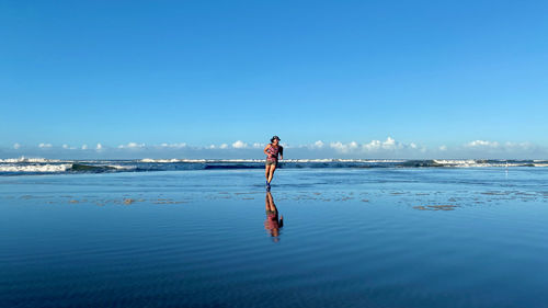 Full length of woman running on beach against clear blue sky