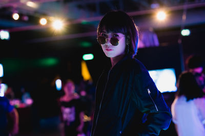 Portrait of young woman standing against illuminated lights at night