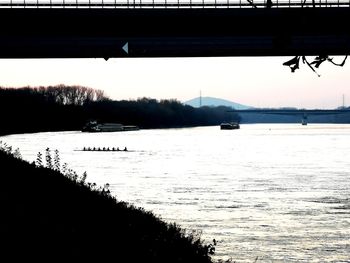 Silhouette bridge over river against sky