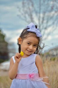 Portrait of smiling girl holding flower while standing on grassy field