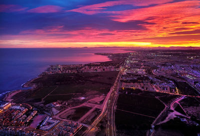 Aerial view of cityscape by sea against sky during sunset