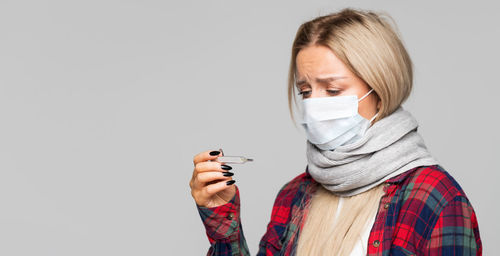 Woman wearing mask holding thermometer against white background