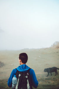 Back view of active touristic person in blue jacket and backpack climbing on ill with dry orange vegetation in spain