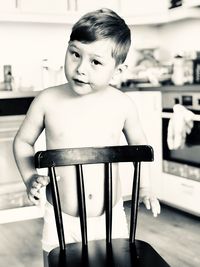 Portrait of shirtless boy standing with chair 