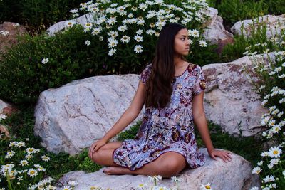 Full length of young woman sitting on rock in park