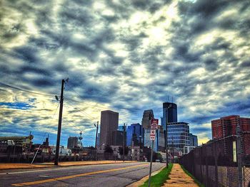 Road passing through city against cloudy sky