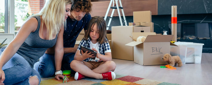 Mother and father looking at son using digital tablet by cardboard boxes at home