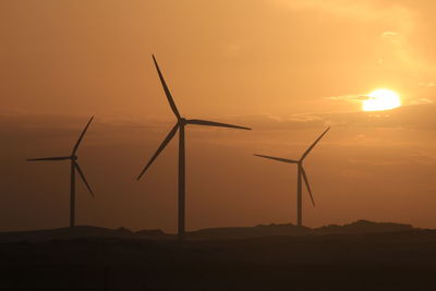 Silhouette wind turbines on landscape against sky during sunset
