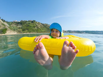 Portrait of boy sitting on pool raft at sea against sky