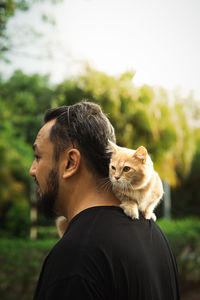 Munchkin cat lays on the neck of a middle age man in the park.