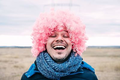 Close-up of happy man wearing wig at beach against sky