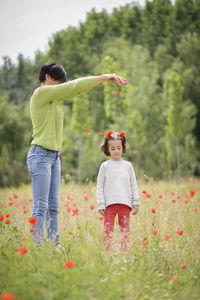 Mother throwing flowers on cute daughter while standing on grassy field