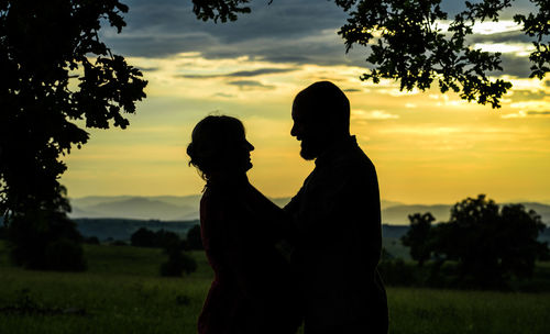 Silhouette couple standing on field against sky during sunset