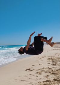 Parkour backflip on beach against clear sky