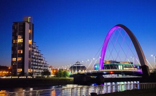 Illuminated bridge over river against sky in city at night