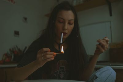 Young beautiful woman with the cigarette and fire match at home