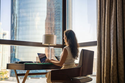 Rear view of woman using laptop at home