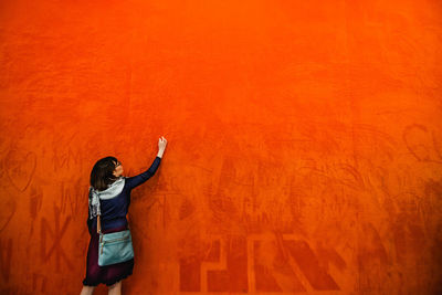 Rear view of woman standing against orange wall