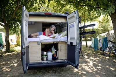 Senior woman lying in camper van reading book