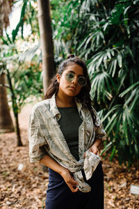 Portrait of young woman wearing sunglasses standing against plants