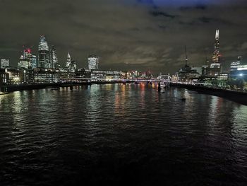 Illuminated buildings by river against sky at night