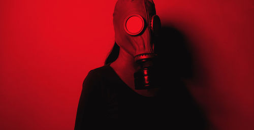 Woman wearing gas mask standing against red wall