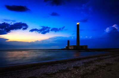 Lighthouse by sea against sky during sunset