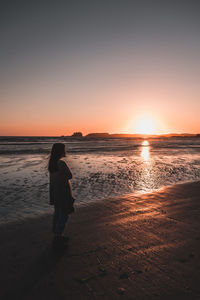 Rear view of woman standing on beach during sunset
