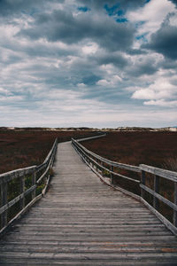 Wooden footbridge on landscape against cloudy sky