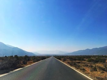 Empty road by mountains against clear blue sky