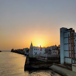 Buildings by sea against clear sky during sunset