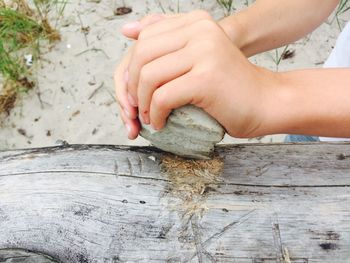 Cropped image of child hand scratching with stone on wood
