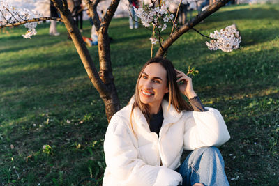 Woman enjoying spring sitting on grass in city park among flowering trees