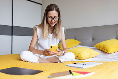 Smiling woman using mobile phone while sitting on bed at home