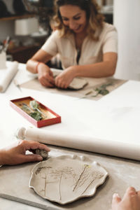 Woman decorating with flowers rolled clay, making ceramic plate in studio with floral pattern