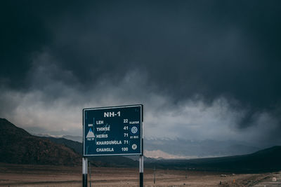 Information sign on road by mountain against sky