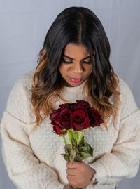 Portrait of young woman holding rose against white wall