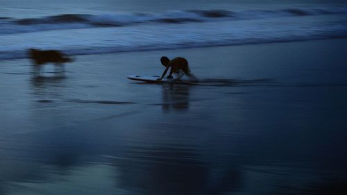 Boy surfboarding on sea at dusk