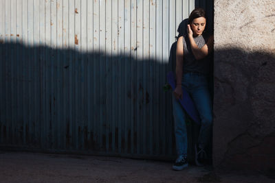 Young woman holding skateboard by gate