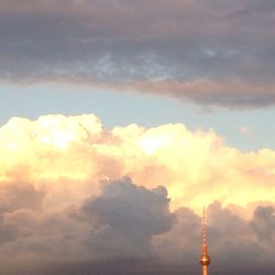 Low angle view of communications tower against cloudy sky