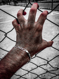 Cropped hand of man holding chainlink fence