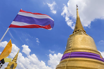 Low angle view of thai flag and pagodas against cloudy sky