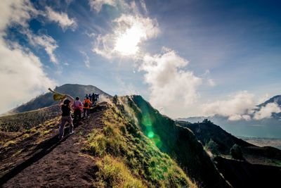 Rear view of people walking on mountain against cloudy sky