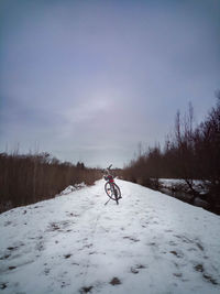 Man riding bicycle on snow covered field against sky