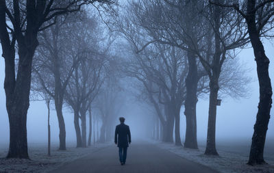 Man walking on road amidst spooky trees