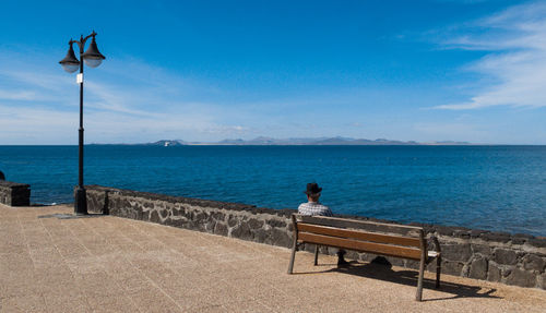 Rear view of man sitting on bench at promenade against blue sky