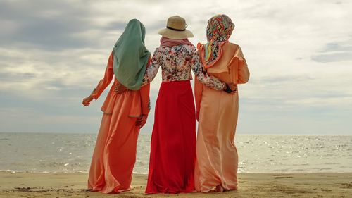 Rear view of people standing on beach against sky