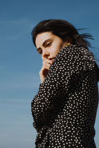 Side view of young woman looking away against sky