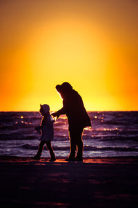 Silhouette mother and daughter beach against sky during sunset